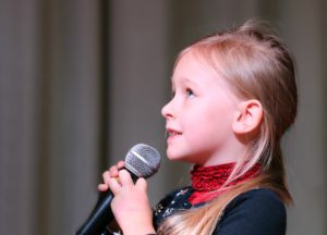 Little girl singing into a microphone; a Spectrum Youth Singers rehearsal is one of the September 8th-14th events happening soon. 