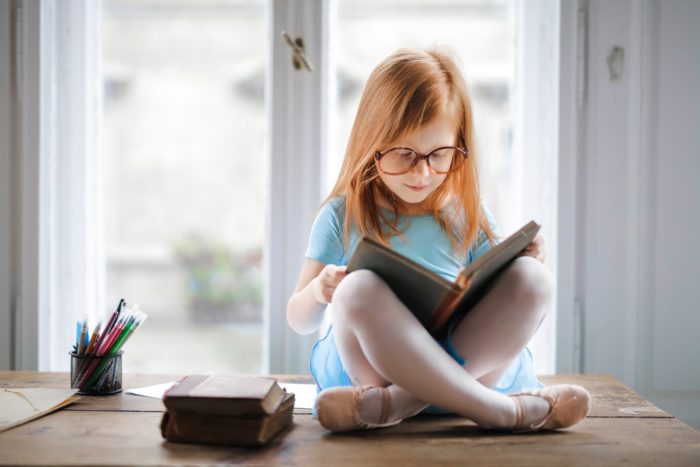 Girl reading a book in front of a window.