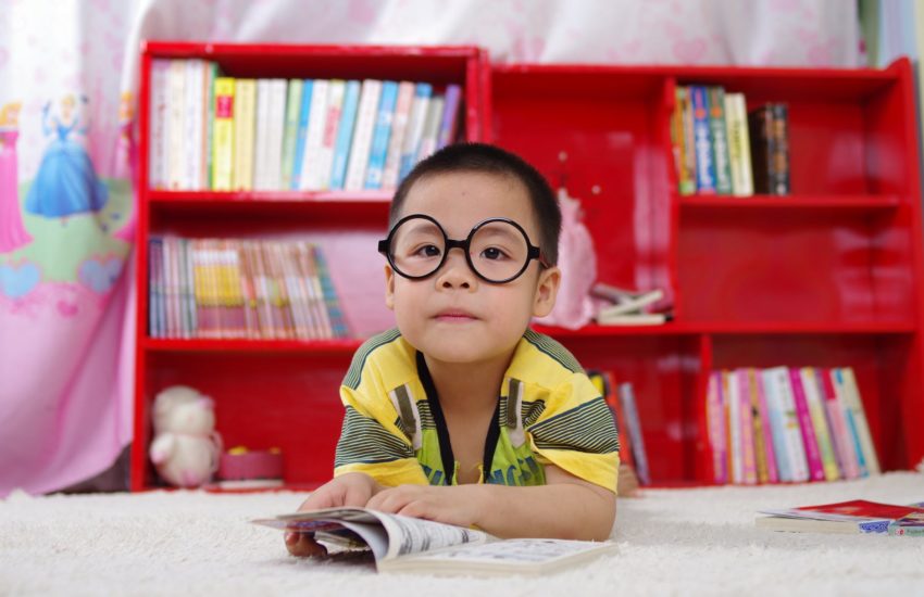 Child wearing glasses reading a book; there are many great local libraries for kids.