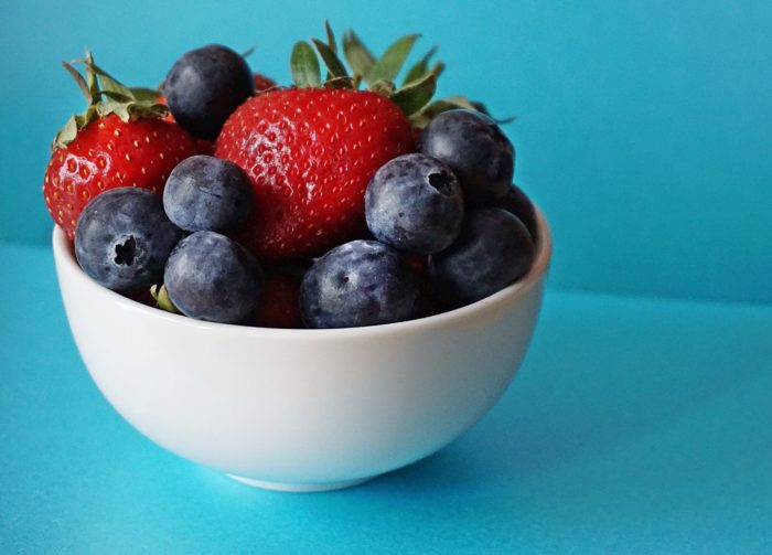 Bowl of strawberries and blueberries against a blue background.