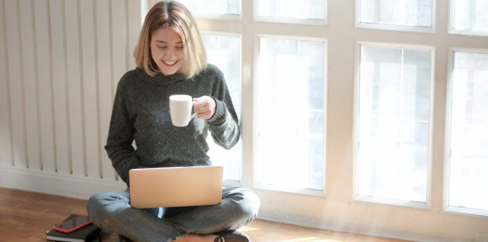 Woman enjoying a cup of coffee while chatting virtually on a computer as part of her self care routine. 