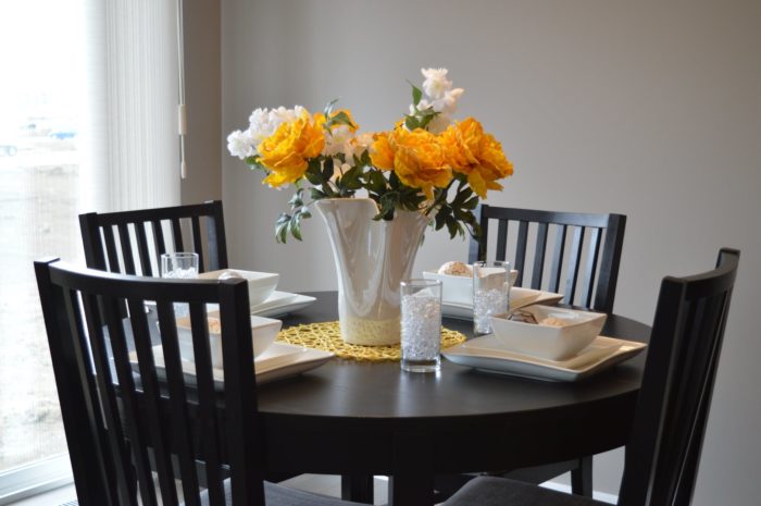Small table and chairs with place settings and a vase of yellow and white flowers.