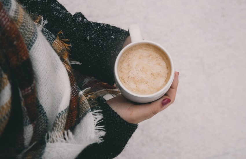 Woman wearing a coat and scarf holding a cup of hot cocoa outside in the snow.
